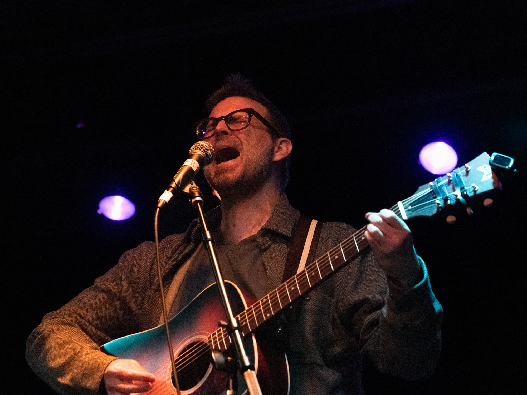 Ian Felton mid-vocal at the microphone, head tilted back, blue stage lights behind