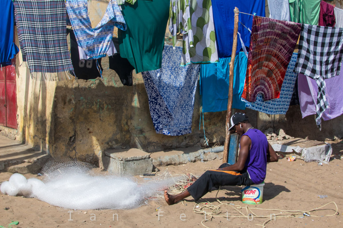 A man repairs fishing nets — a critical job in the fishing village